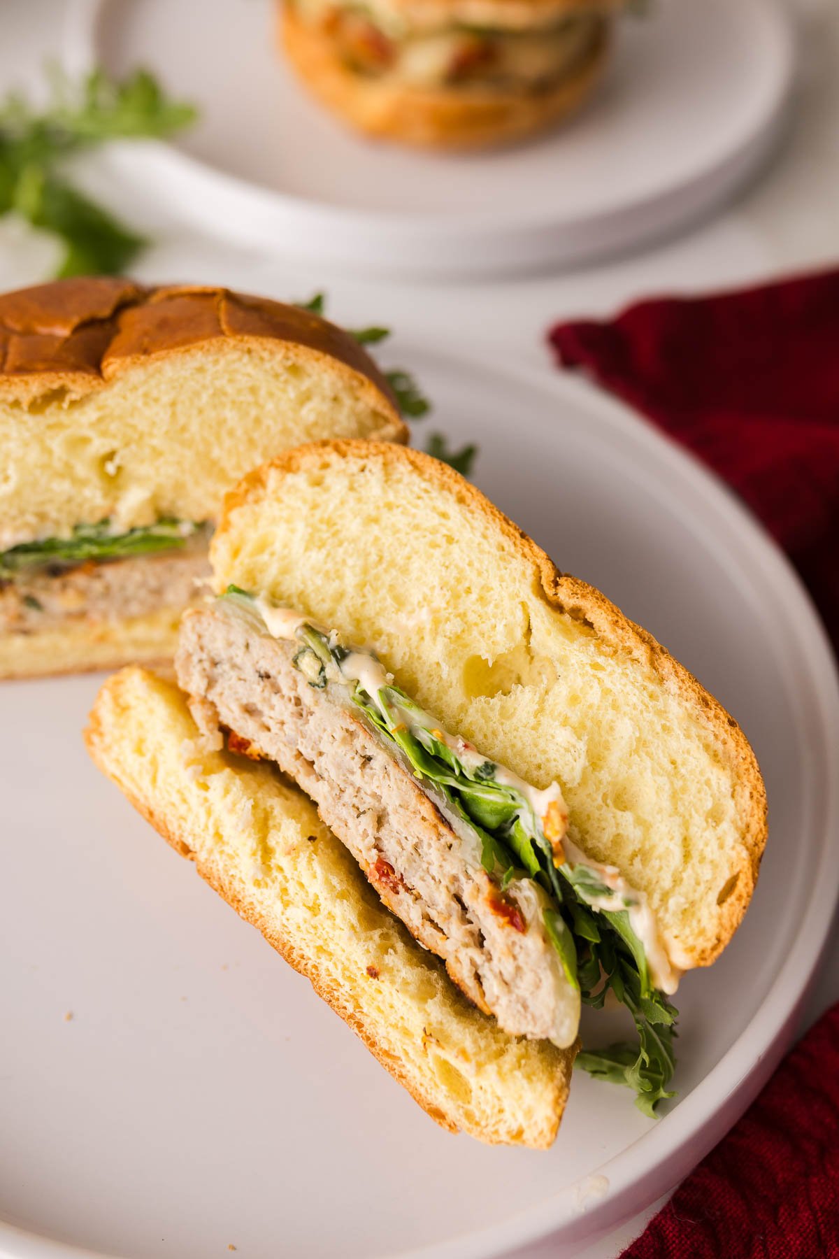 A sliced chicken slider with lettuce and sauce on a bun, served on a white plate.