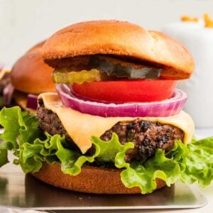 A cowboy butter hamburger with lettuce, tomato, pickles, onion, and a beef patty on a bun is placed on a white plate.