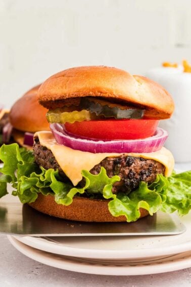 A cowboy butter hamburger with lettuce, tomato, pickles, onion, and a beef patty on a bun is placed on a white plate.