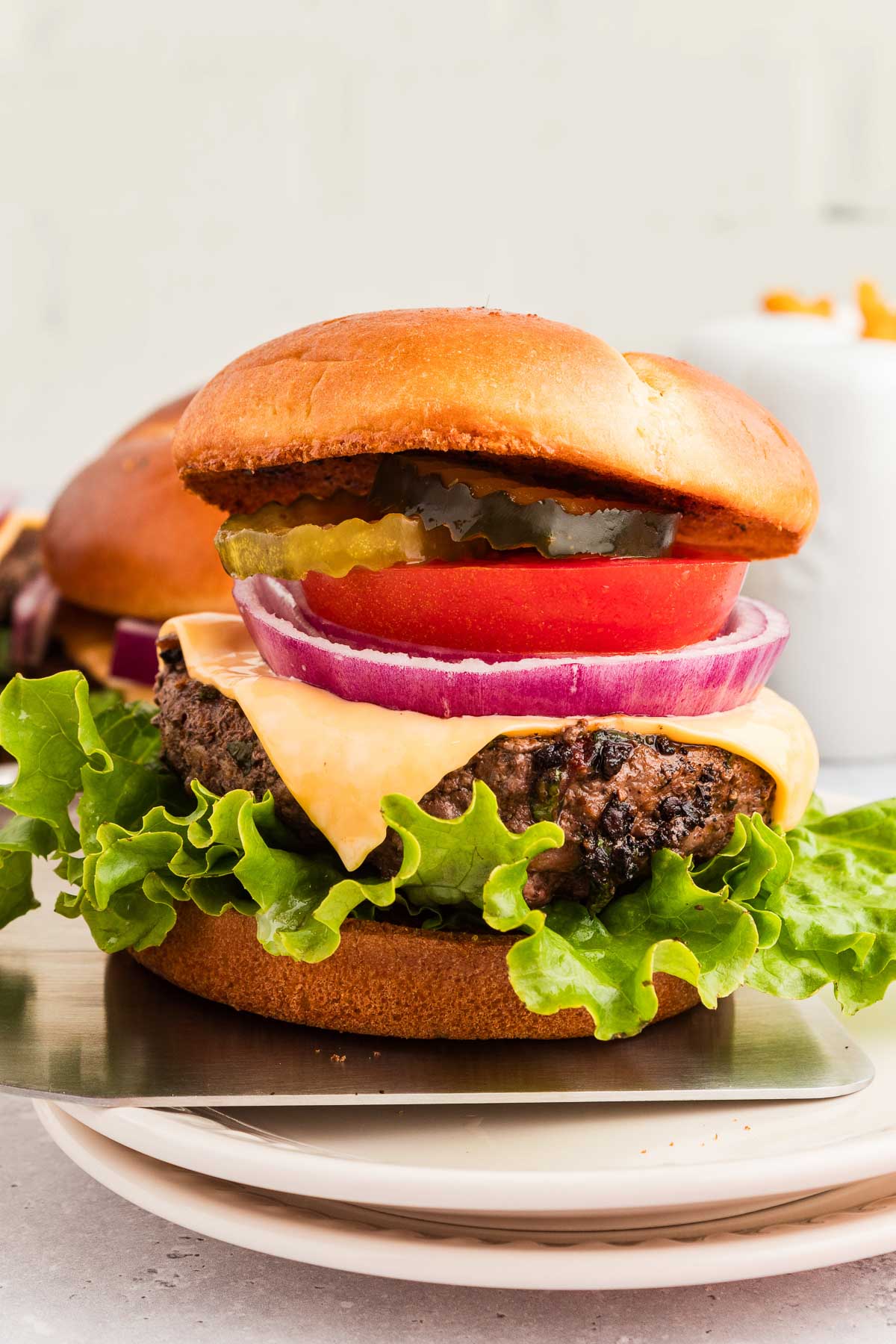 A cowboy butter hamburger with lettuce, tomato, pickles, onion, and a beef patty on a bun is placed on a white plate.