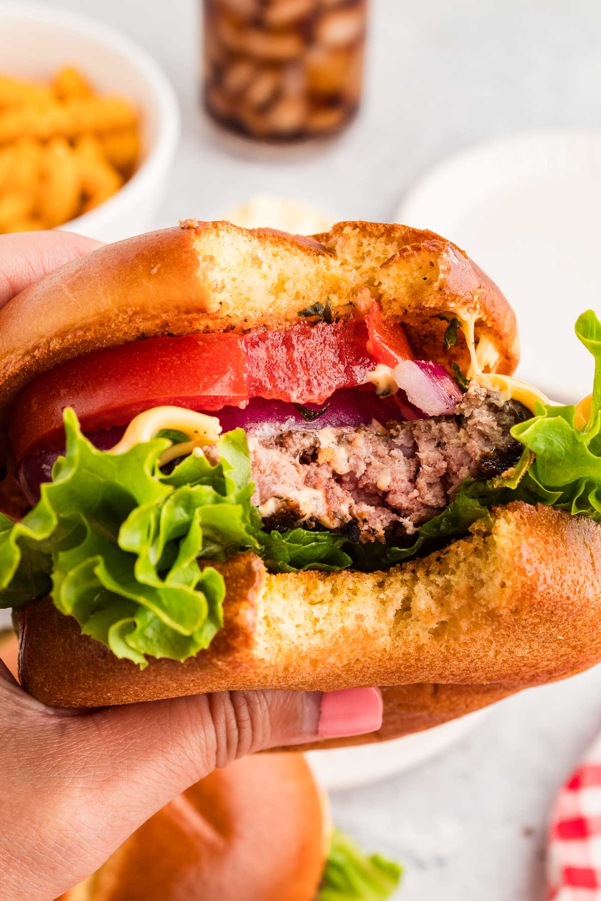 A hand holding a partially eaten cowboy butter burger with lettuce, tomato, red onion, cheese, and a beef patty in a bun.