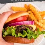 A hand holding a burger and fries.