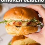 A hand holding a chicken slider with melted cheese and greens on a bun, with another slider on a plate in the background. Text reads, “How to Make Marry Me Chicken Sliders.”.