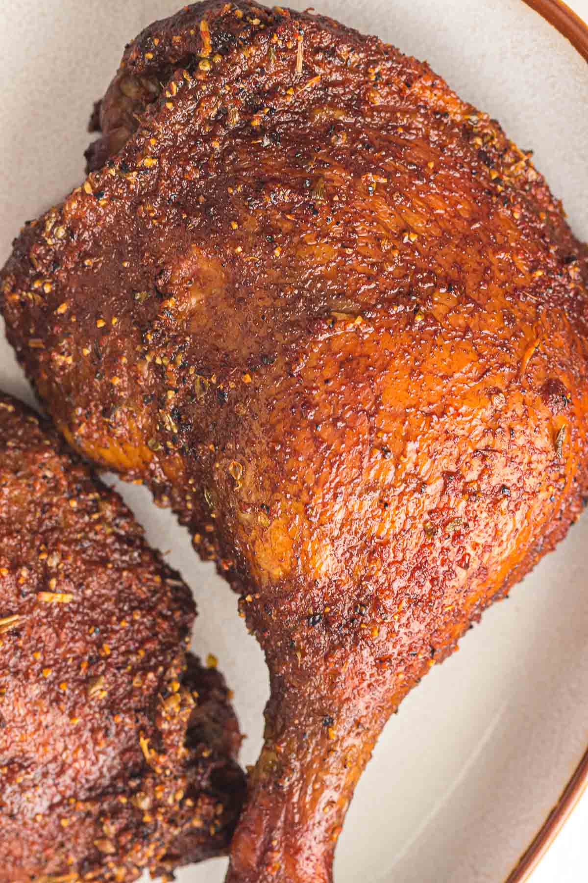 Close-up of a smoked, seasoned duck leg quarter with crispy skin on a white plate.