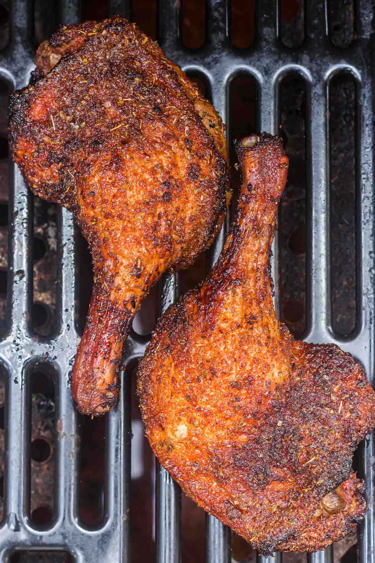 Two seasoned duck leg quarters grilling on a barbecue grate.