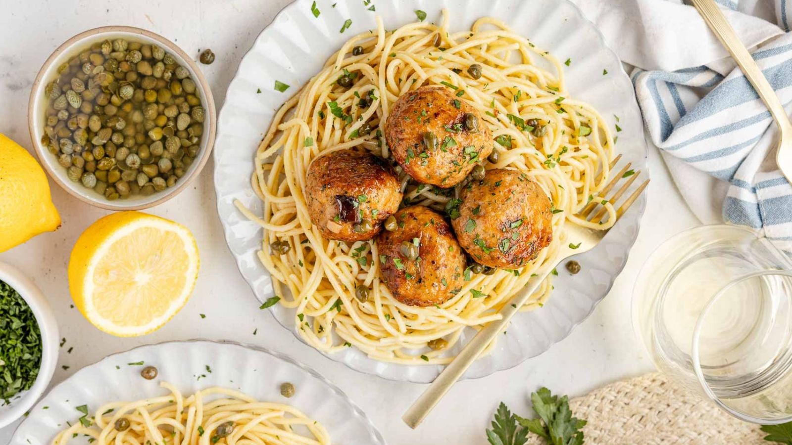 Chicken piccata meatballs coated in lemon butter sauce with capers scattered around.