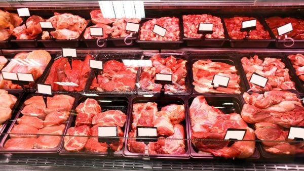 Display case filled with various cuts of raw meat arranged in black trays, each labeled with blank white tags under bright lighting.