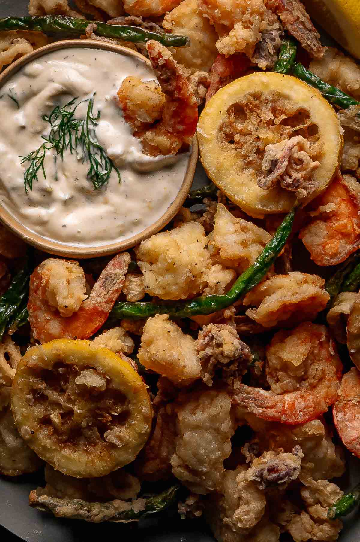 Fritto misto: a close up of plate of assorted fried seafood and vegetables with a small bowl of creamy tartar sauce garnished with fresh dill.