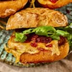 Close-up of a Gochujang Chicken Burger with melted cheese and kimchi bacon jam on a rustic bun, placed on a ceramic plate.