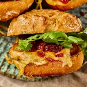 Close-up of a Gochujang Chicken Burger with melted cheese and kimchi bacon jam on a rustic bun, placed on a ceramic plate.