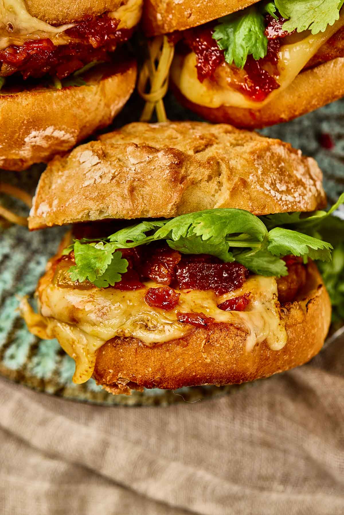 Close-up of a Gochujang Chicken Burger with melted cheese and kimchi bacon jam on a rustic bun, placed on a ceramic plate.