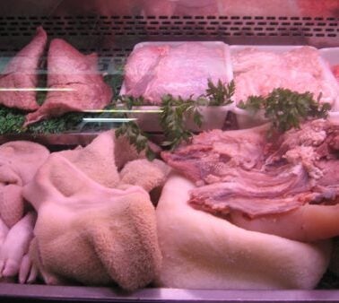 Display case with various cuts of raw meat including tripe, pig's feet, offal, and ground meat, garnished with parsley.