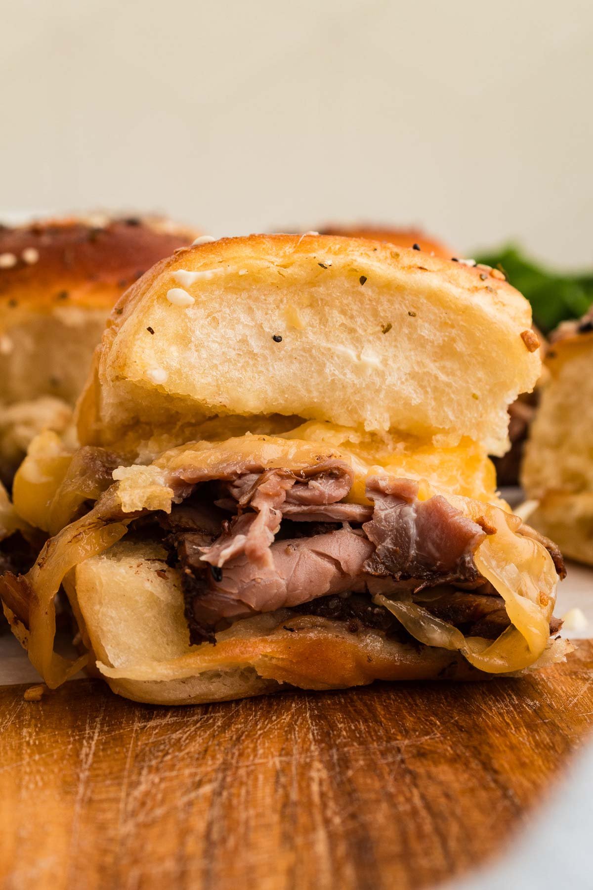 A close-up of a roast beef sliders with sliced roast beef, melted cheese, and on a Hawaiian slider bun, placed on a wooden surface.