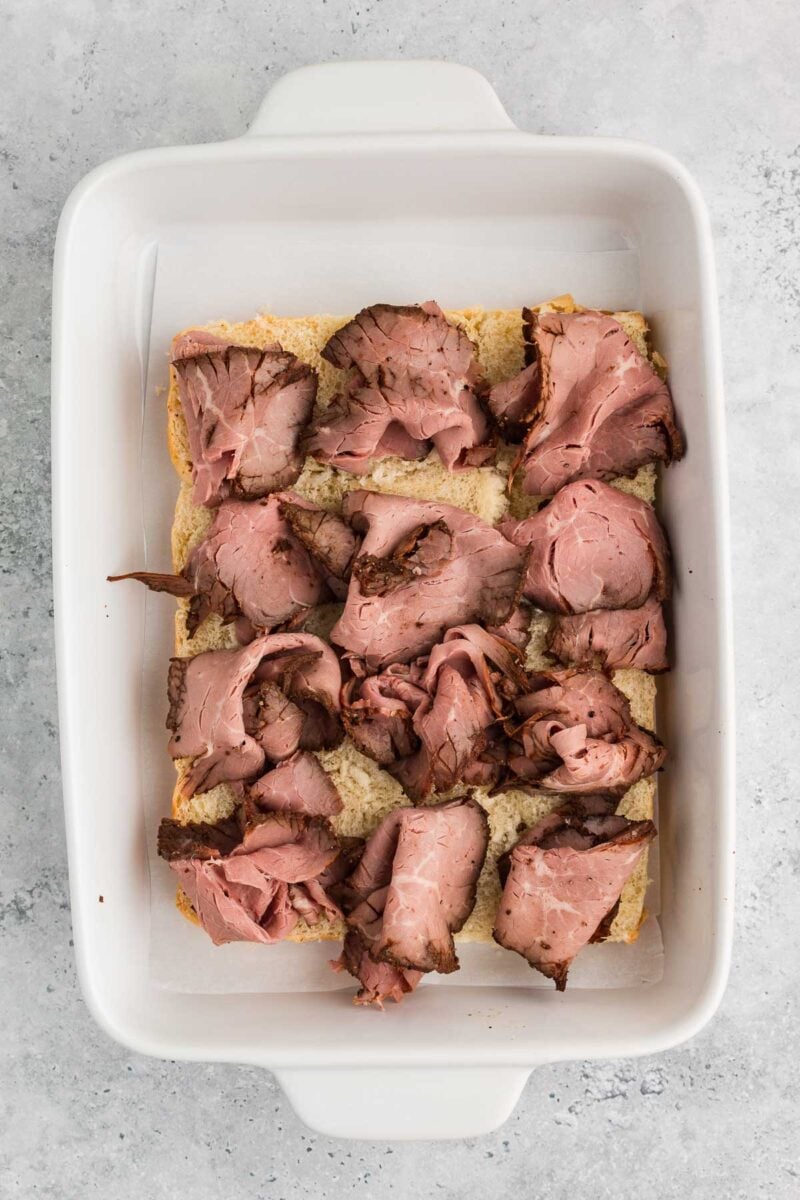 A white baking dish containing slices of roast beef arranged on top of pieces of bread.