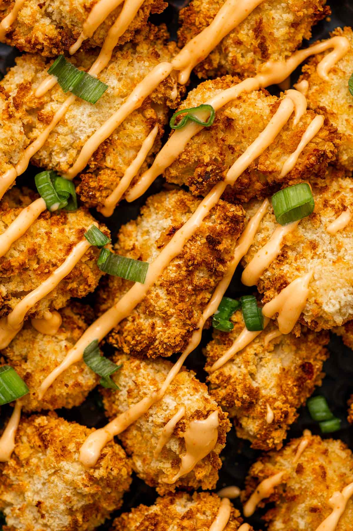 Golden-brown breaded bang bang chicken nuggets drizzled with bang bang sauce and garnished with sliced green onions.