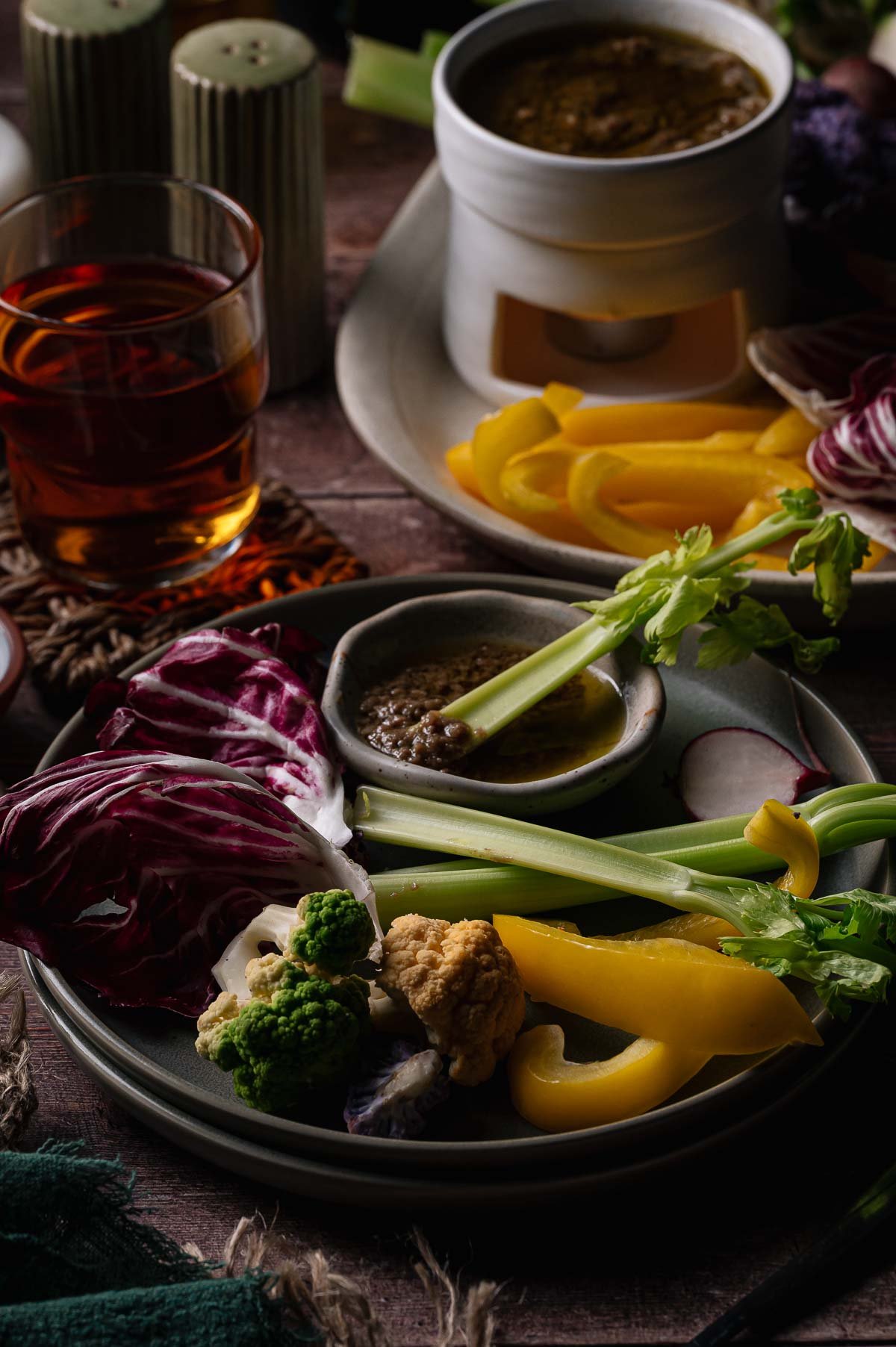 A plate of assorted raw vegetables, including celery, radicchio, cauliflower, broccoli, and yellow bell pepper, served with Bagna cauda dipping sauce.