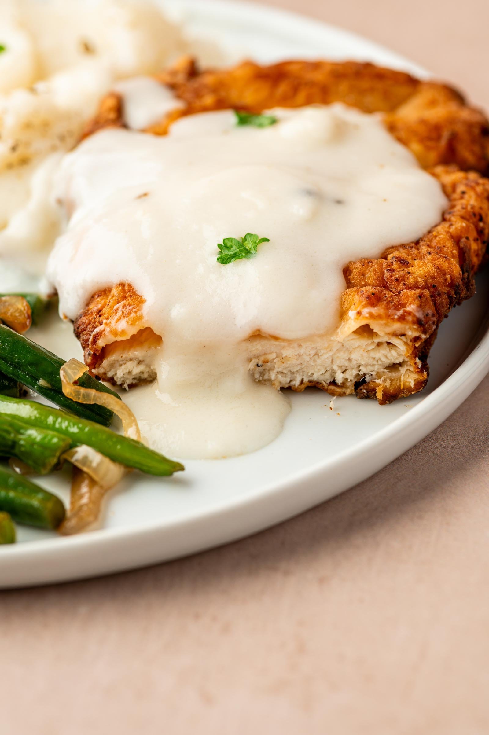 A plate of chicken fried chicken topped with white gravy, served with mashed potatoes and green beans.