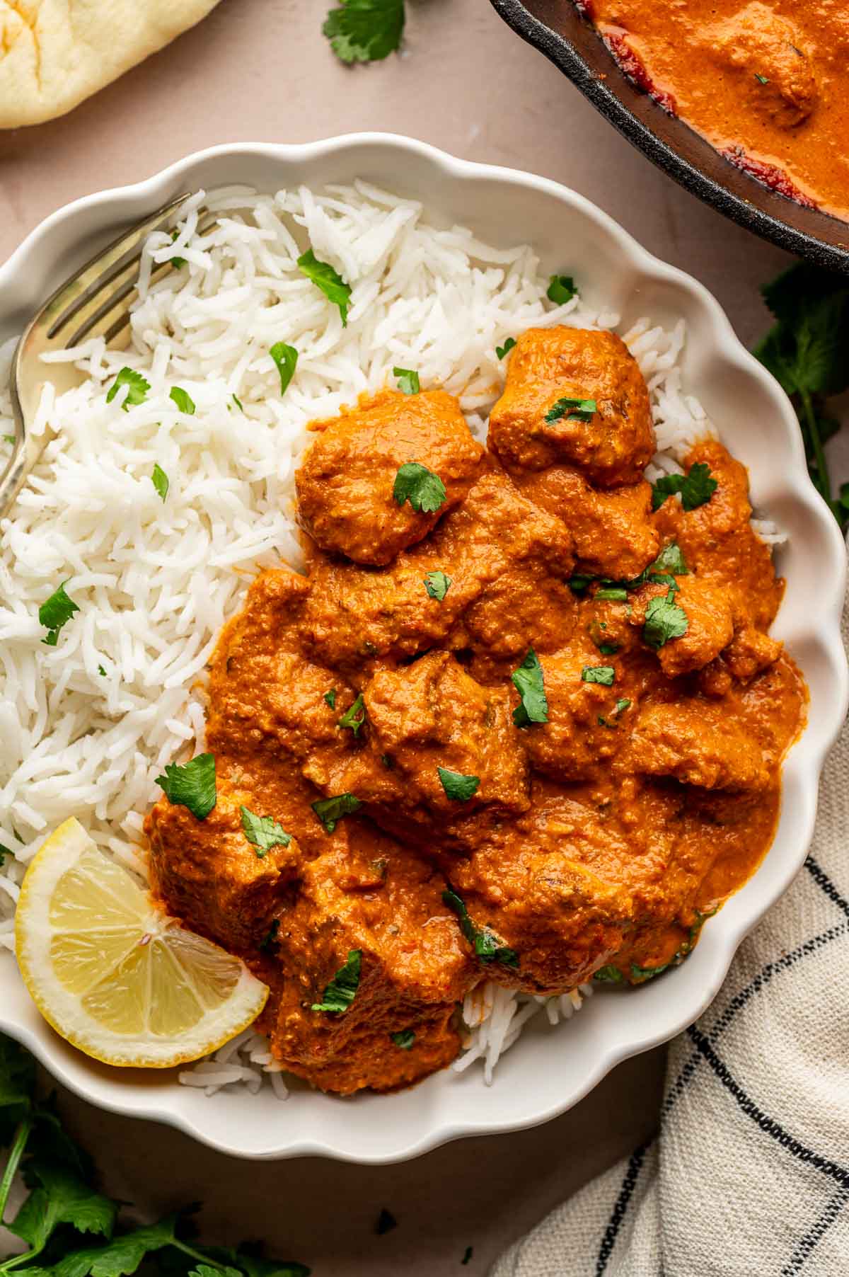 A white bowl filled with steamed white rice and orange chicken tikka masala, garnished with chopped cilantro and a lemon wedge.