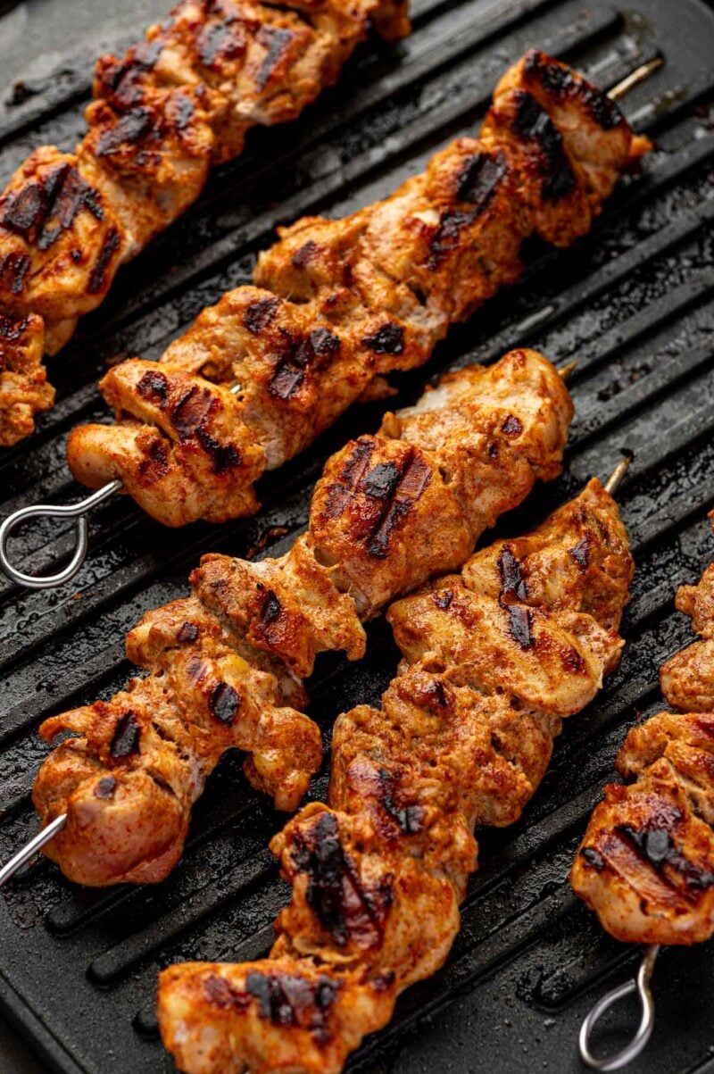 Close-up of grilled chicken skewers with char marks on a ridged grill pan.