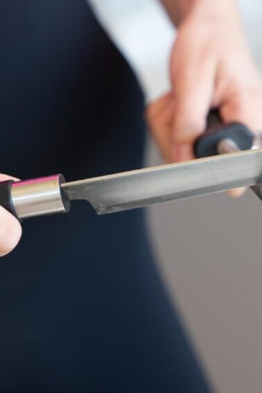 A person holding a knife in one hand and sharpening it with a honing rod in the other hand.