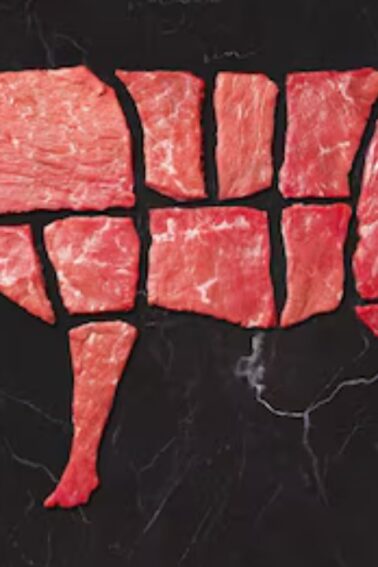 Raw beef cuts arranged on a dark surface in the shape of a cow, illustrating different meat sections.