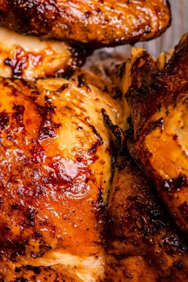 Close-up of two pieces of roasted chicken with crispy, browned skin on a metal tray.