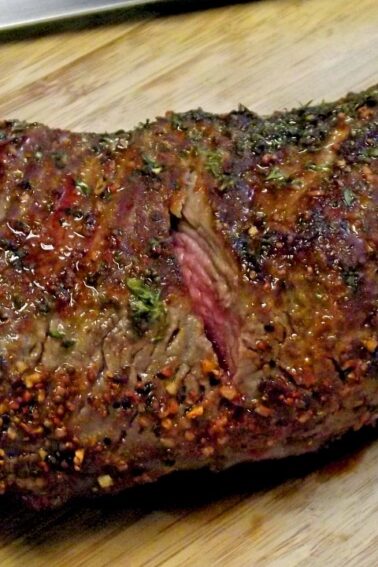 A seasoned and cooked beef tri-tip roast rests on a wooden cutting board, showing a browned exterior with visible herbs and spices.