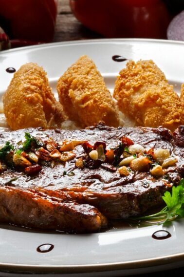 Grilled steak topped with herbs and garlic, served with four scoops of mashed potatoes on a white plate, garnished with sauce dots and fresh parsley.