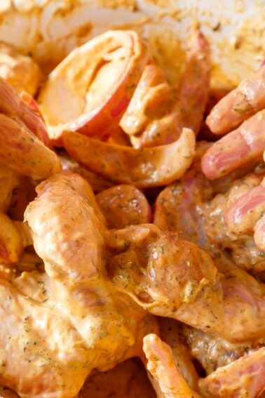 Hands coating raw chicken wings with a seasoned marinade in a white bowl.