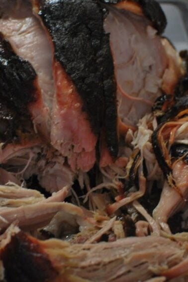 A tray of smoked pulled pork with a dark bark and shredded pieces, showing both the interior and exterior of the meat.