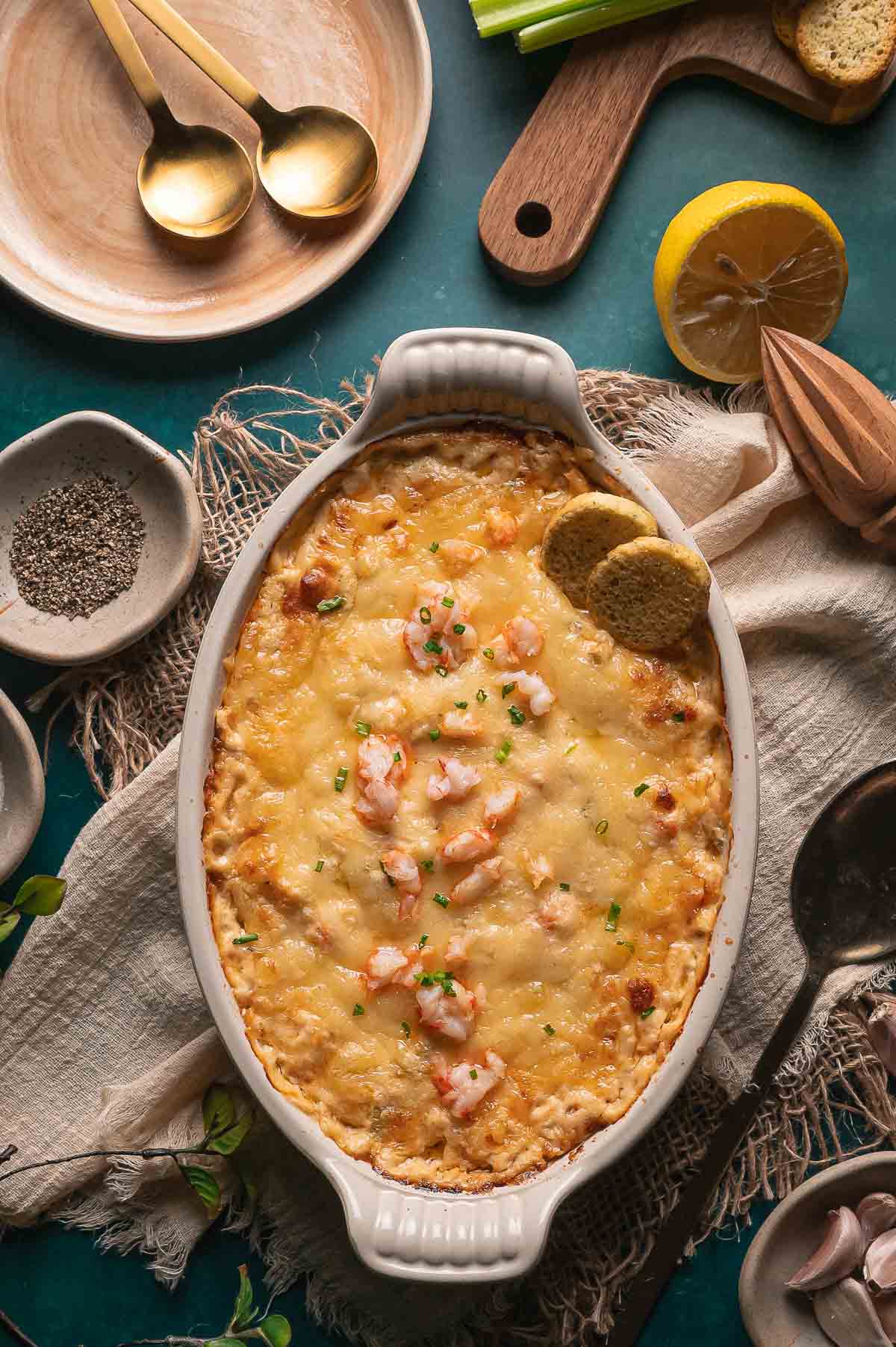 A baked cheesy hot lobster dip, garnished with herbs and served with two round toasted bread pieces in a white oval dish.