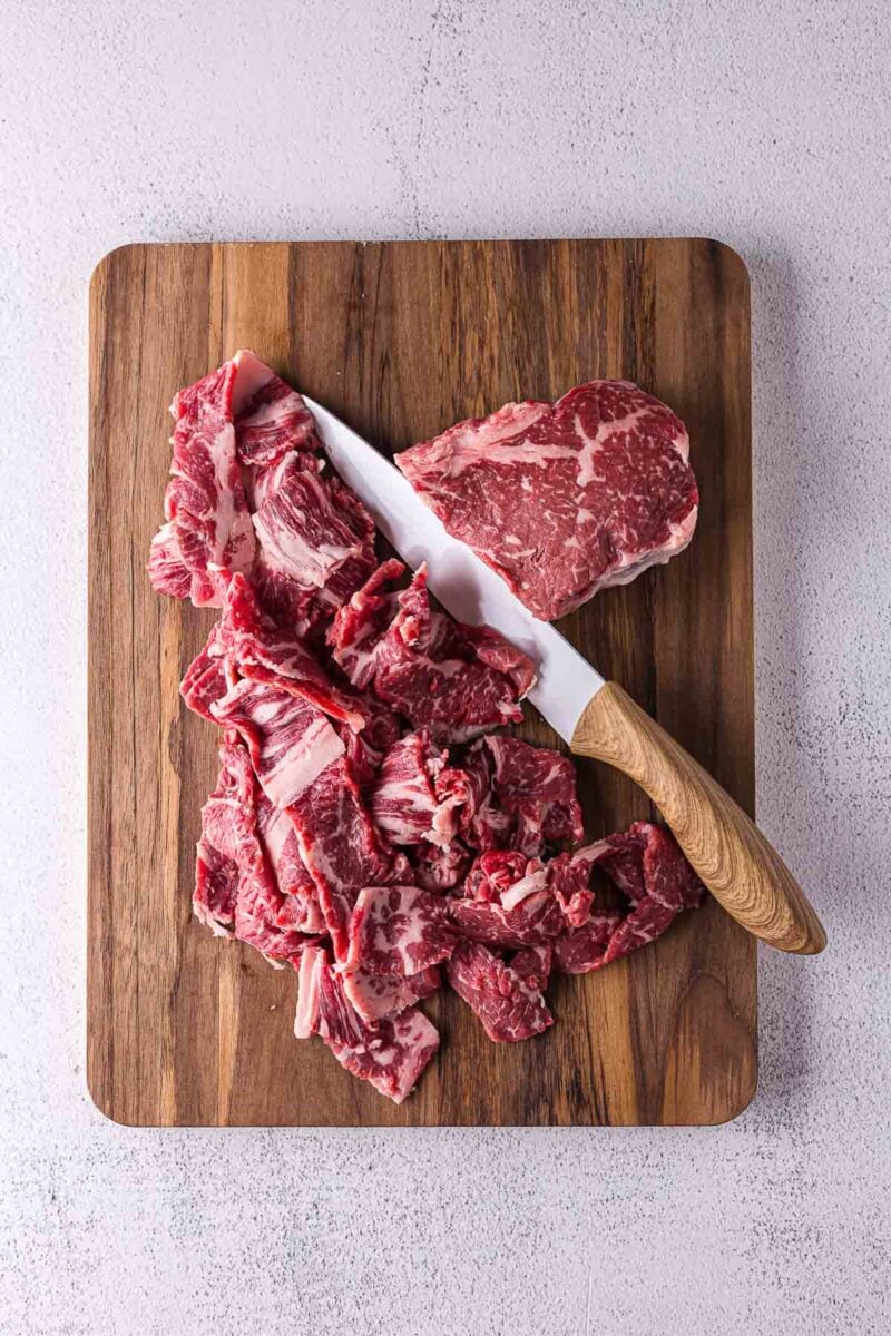 Sliced raw beef and a knife on a wooden cutting board.