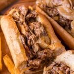 A close-up of a cheesesteak sandwich filled with sliced beef, melted cheese, and cooked onions, served with French fries.
