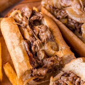 A close-up of a cheesesteak sandwich filled with sliced beef, melted cheese, and cooked onions, served with French fries.
