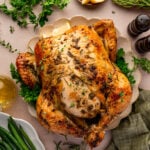 Roast chicken garnished with herbs on a platter, surrounded by lemon wedges, green beans, parsley, rosemary, salt and pepper shakers, and a green napkin.