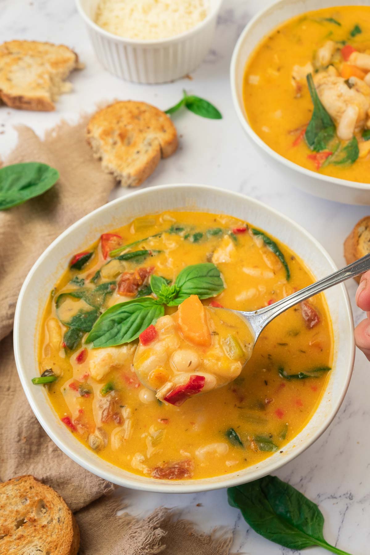 A bowl of creamy tuscan white bean soup and bean soup with chicken and spinach, garnished with basil, served with toasted bread slices on the side.