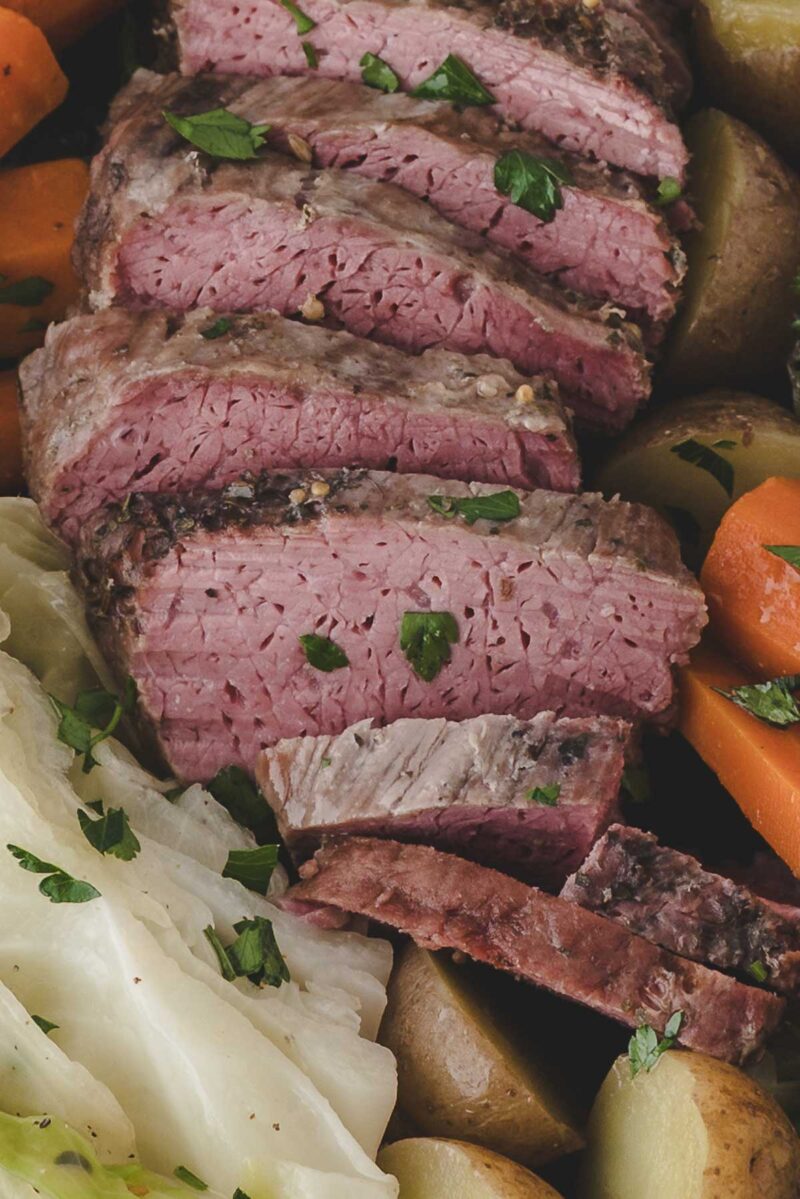 Sliced corned beef garnished with parsley, served with boiled potatoes, carrots, and cabbage.