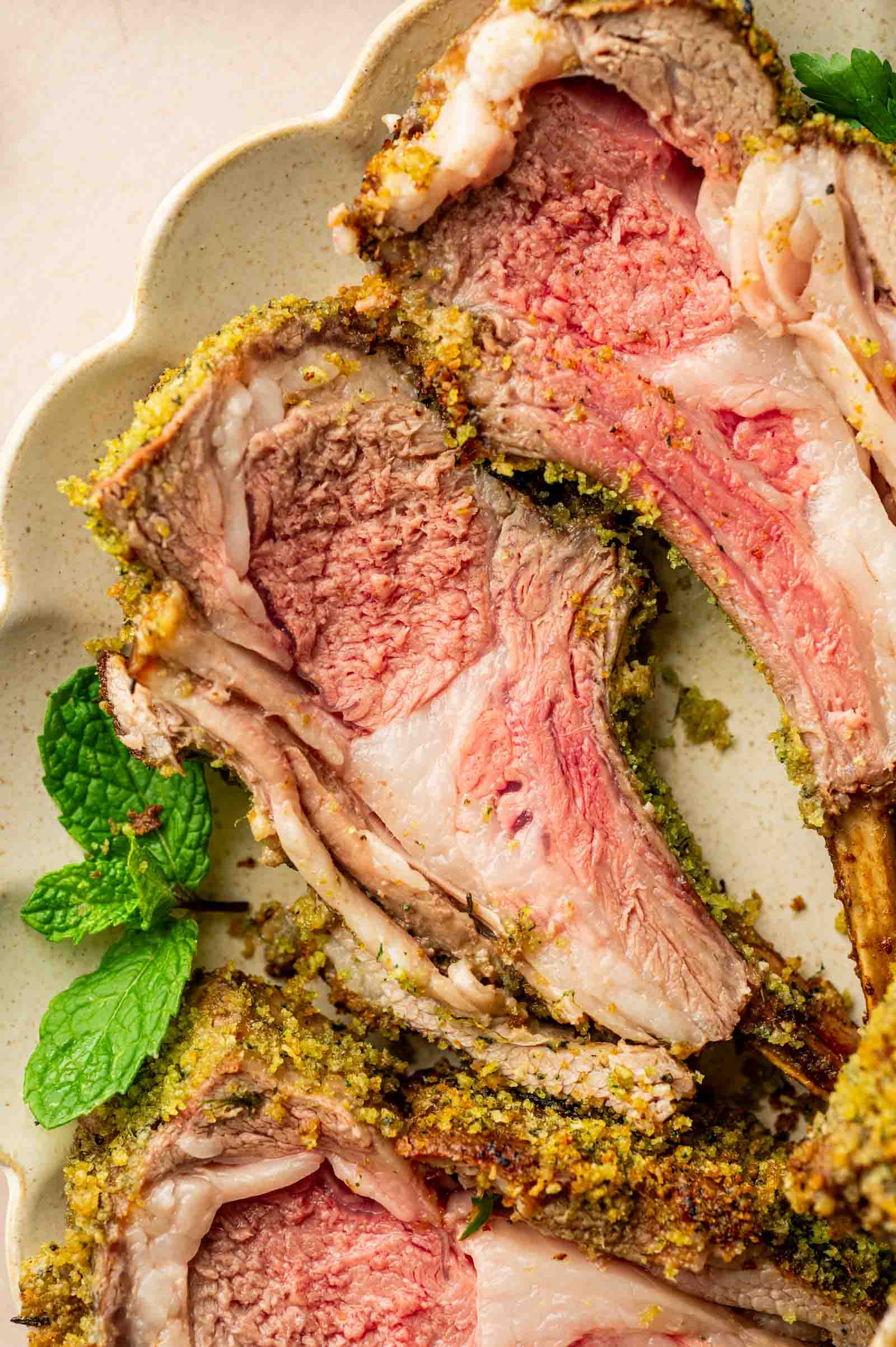 Sliced rack of lamb cooked medium-rare with a herb crust, served on a plate with fresh mint leaves.