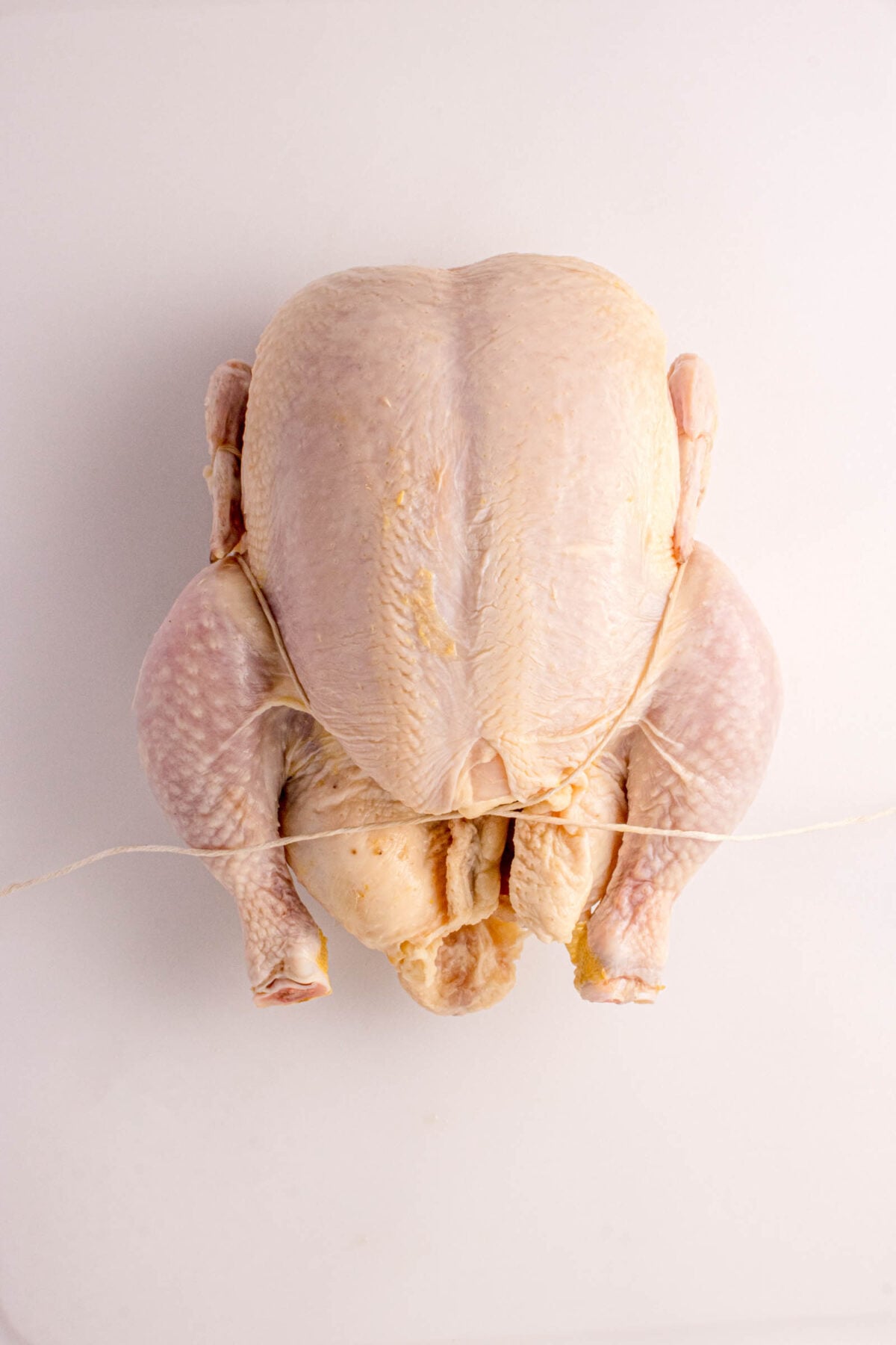 Raw whole chicken with legs tied together, placed on a white surface.