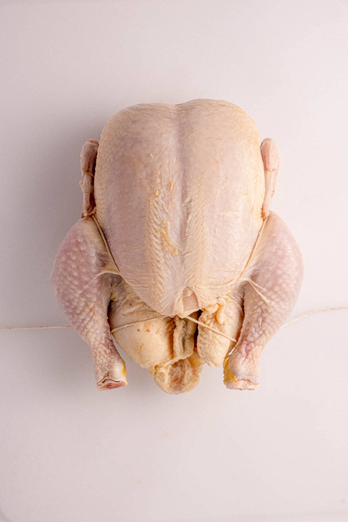 Raw whole chicken placed on a white surface, viewed from above.