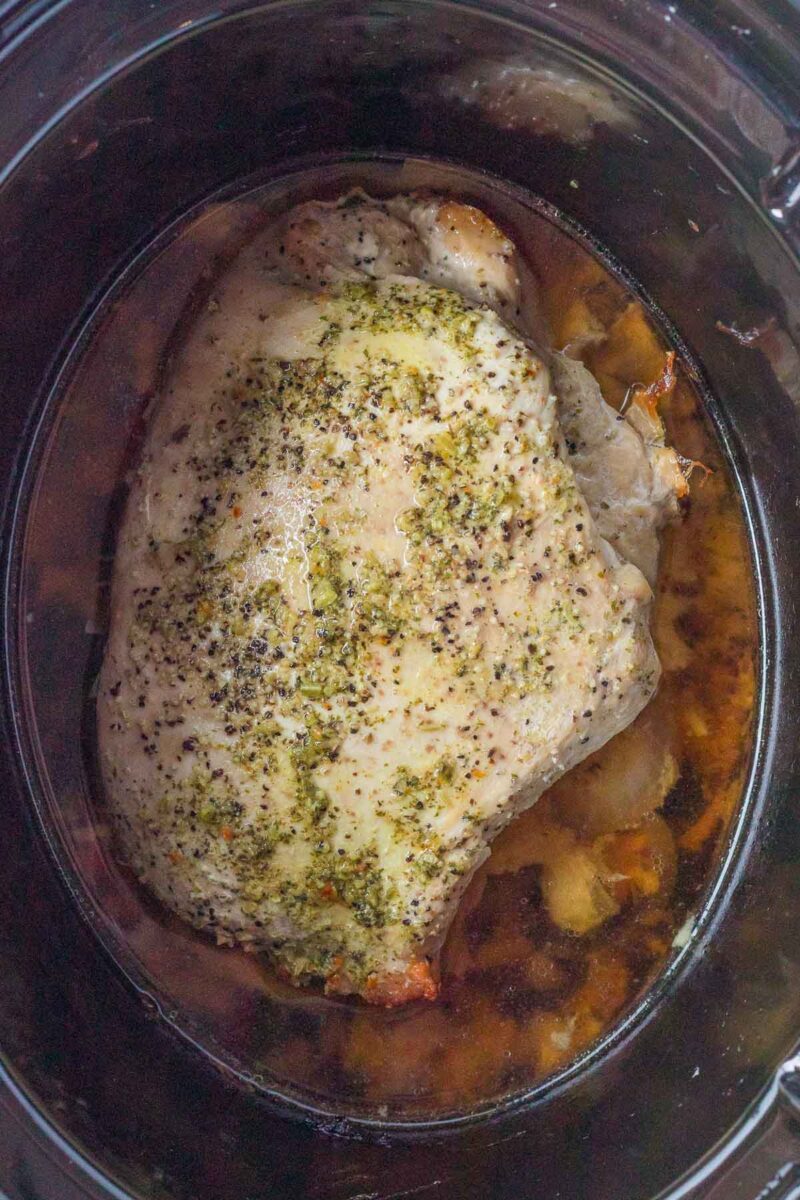 A seasoned boneless turkey breast cooking in a slow cooker, surrounded by its juices.