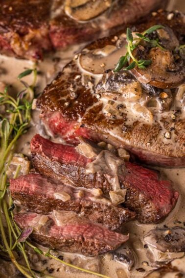 Close-up of sliced steak with a creamy mushroom sauce, garnished with herbs, showing a medium-rare interior.