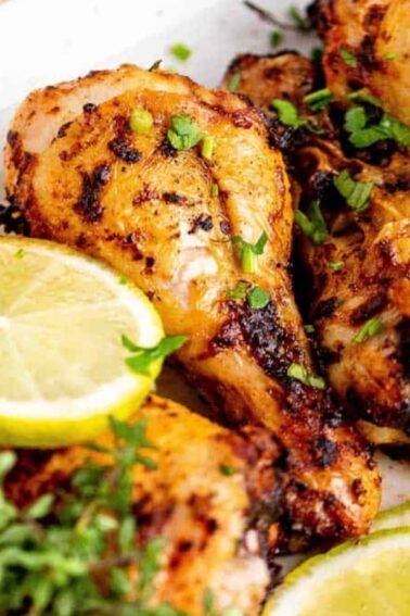 Grilled chicken drumsticks garnished with fresh chopped herbs and lemon slices on a white rectangular plate.