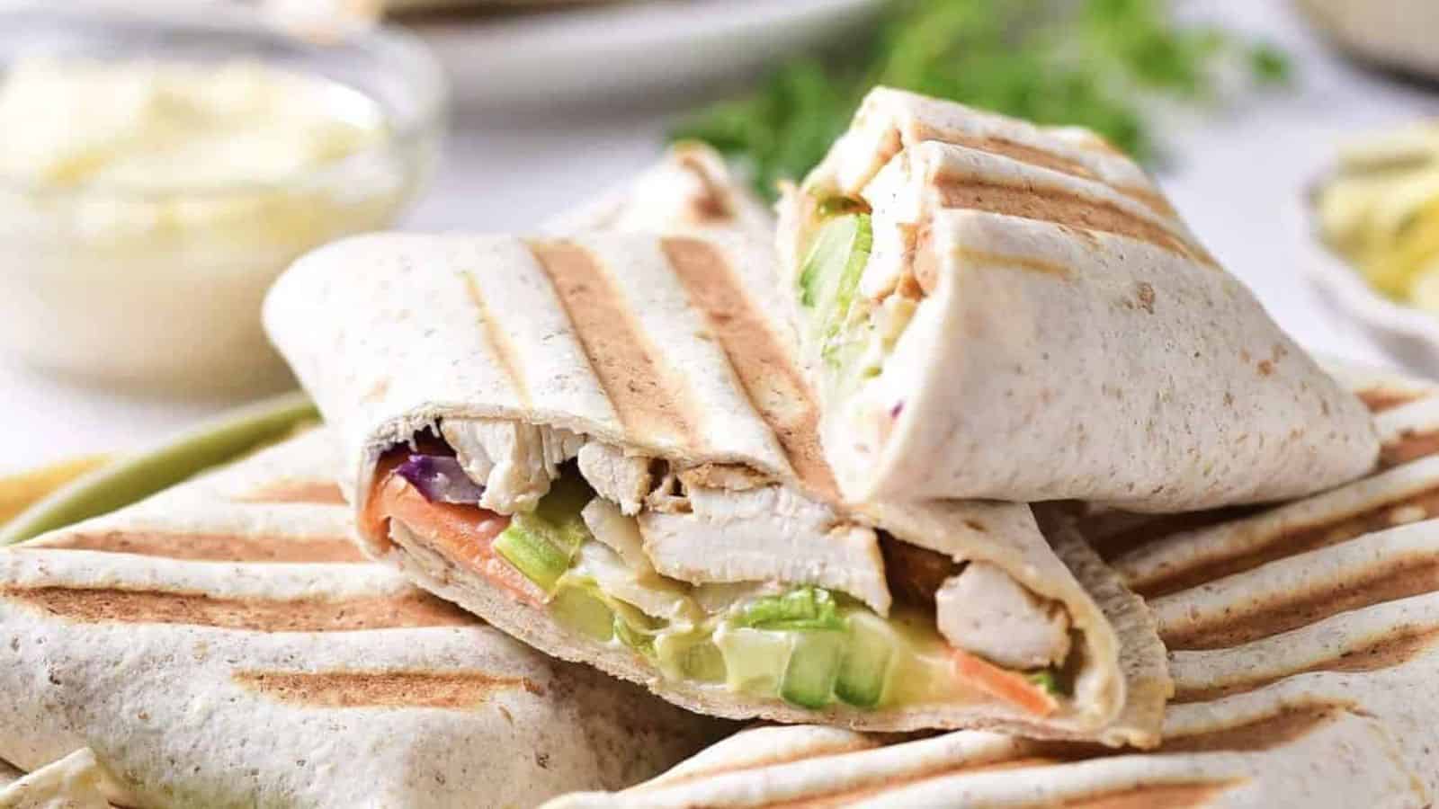 Grilled wraps filled with sliced chicken, lettuce, cucumber, and carrots, stacked on a plate with grill marks visible on the tortillas.