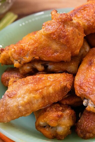 A green plate filled with crispy chicken wings, served with carrot and celery sticks on a wooden surface.