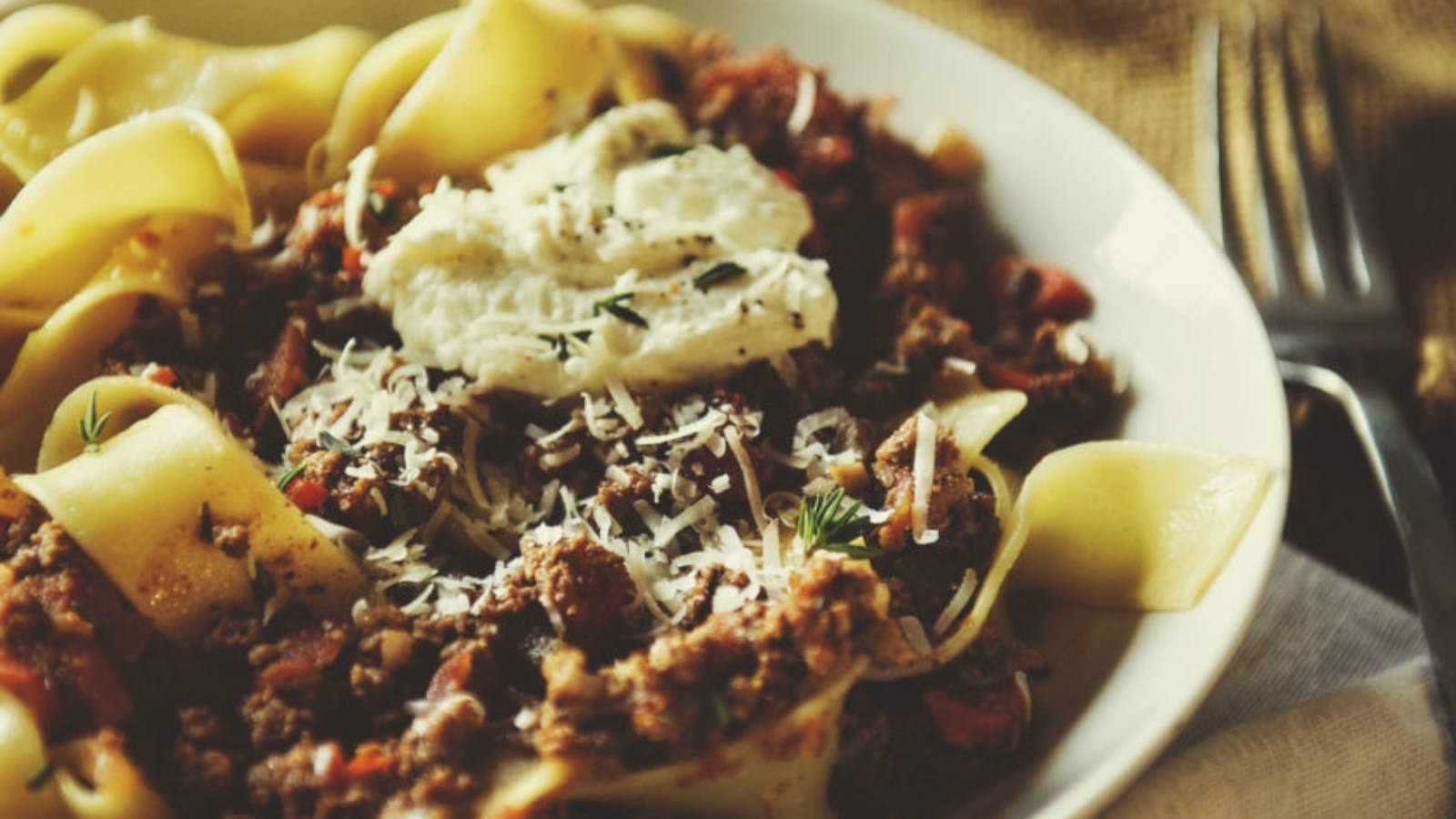 A bowl of pasta with meat sauce, topped with grated cheese and a dollop of ricotta.