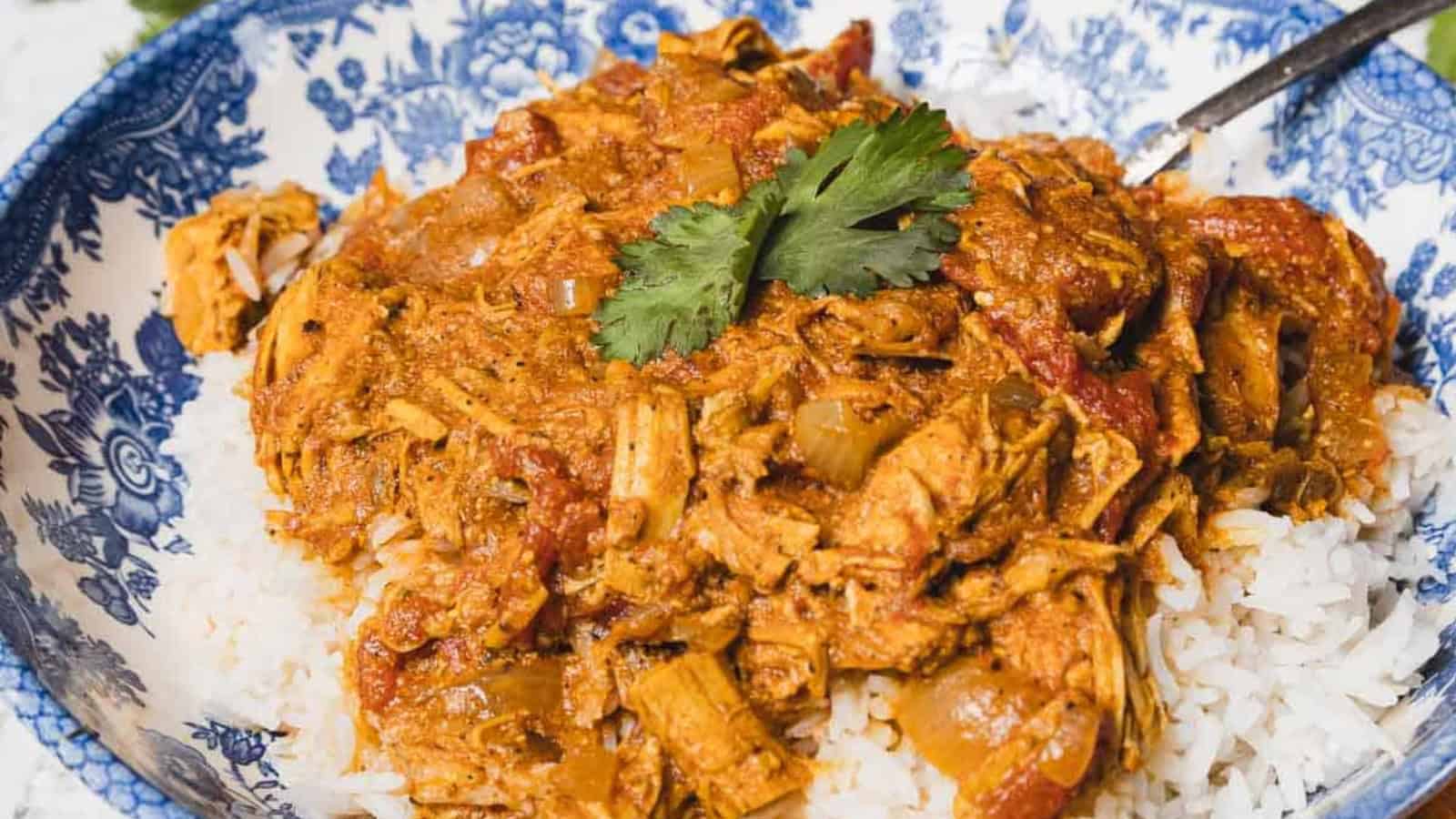 Shredded chicken in a tomato-based sauce served over white rice, garnished with cilantro, on a blue and white patterned plate.