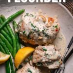 A plate with crab stuffed flounder topped with creamy sauce, green beans, and lemon wedges, with a fork and knife on the side.