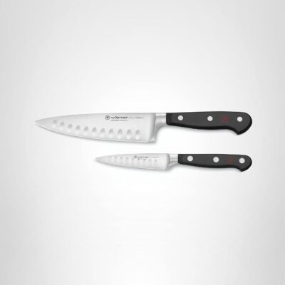 Two kitchen knives with black handles and stainless steel bladesโa larger chef's knife above a smaller paring knifeโare displayed on a light background, perfect for learning how to carve a prime rib with precision and ease.