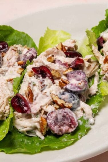 Three lettuce leaves filled with a creamy chicken salad mixture containing grapes and pecans, served on a white oval plate.